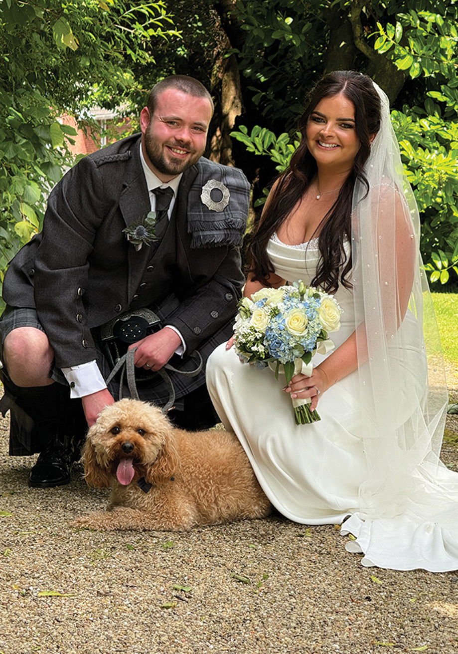 Bride and groom crouched down smile with dog